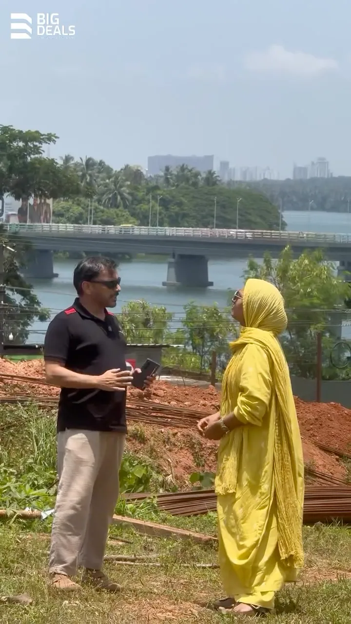 Two presenters on the Sobha Bellevue site in Feroke, with the Chaliyar river and the Feroke bridge behind them