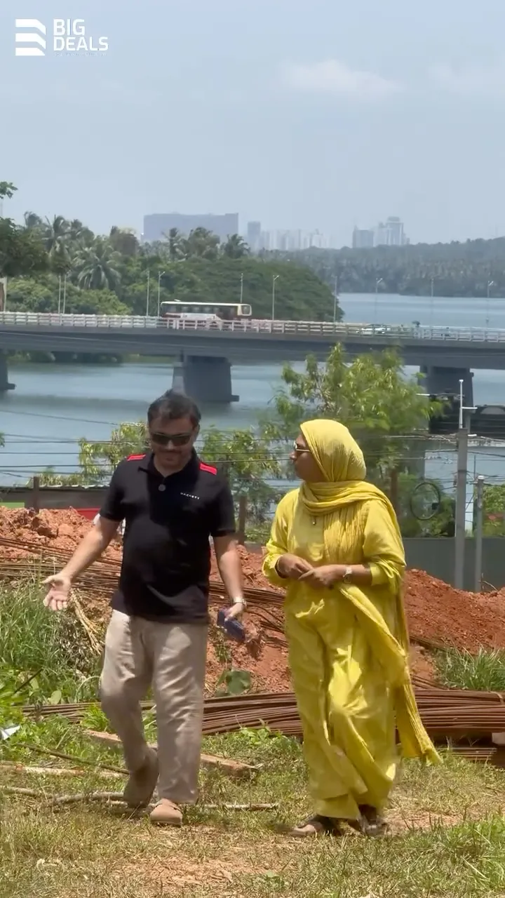 Two presenters walk across the Sobha Bellevue plot, with the Chaliyar and the Feroke bridge behind them
