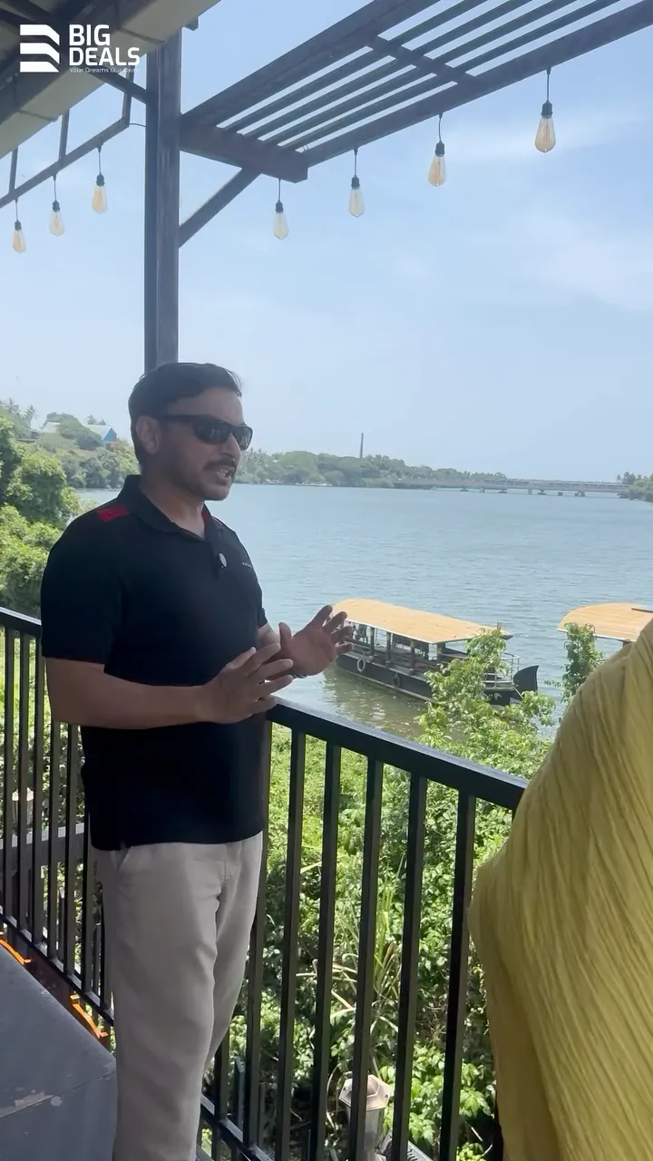 A presenter on a balcony above the river in Feroke, with boats moored below, in Big Deals' Sobha Bellevue film