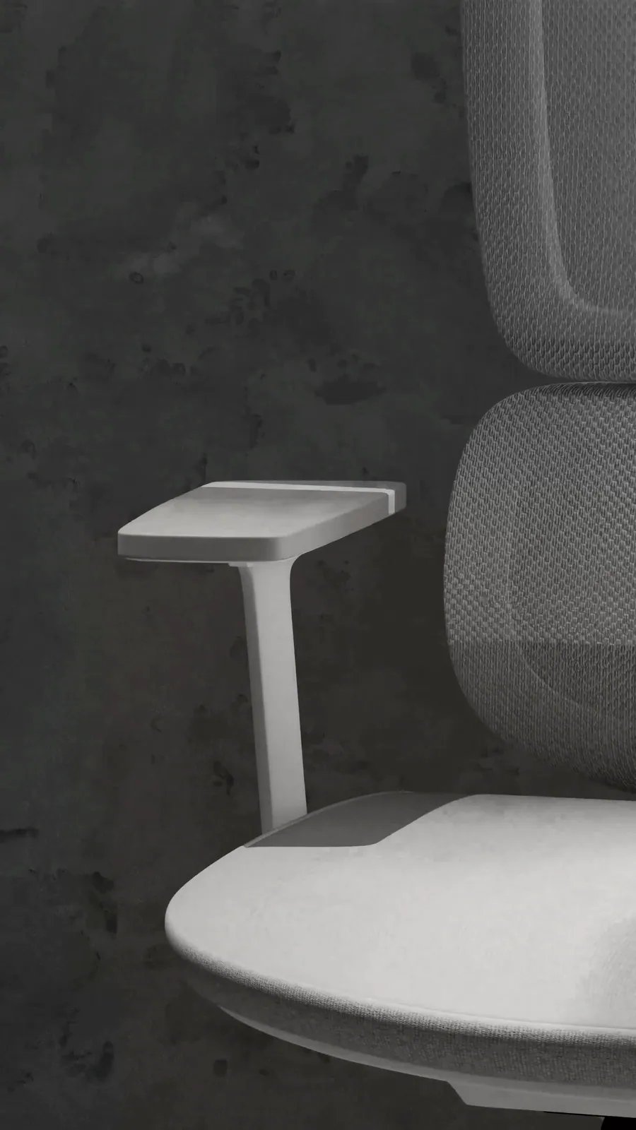 Close-up of the grey chair's white armrest and mesh back in a dark room