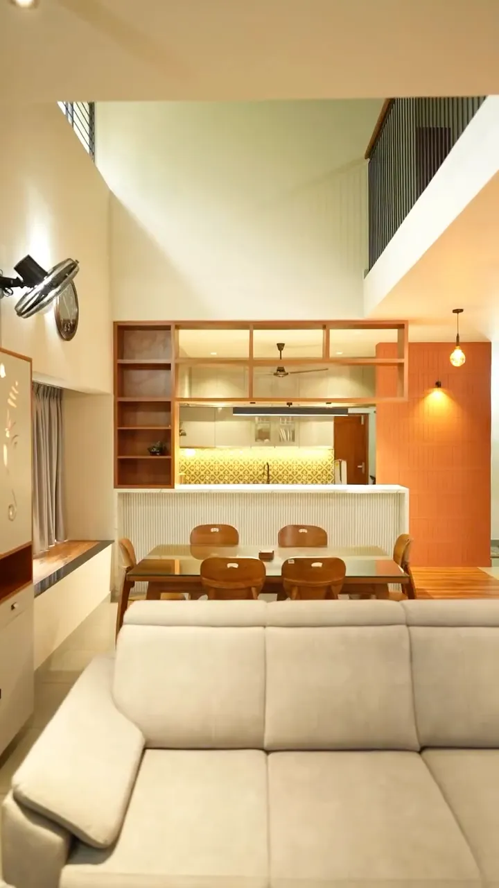 Inside a Hiline home: a double-height living room with a dining table, and a kitchen behind a wooden shelf wall