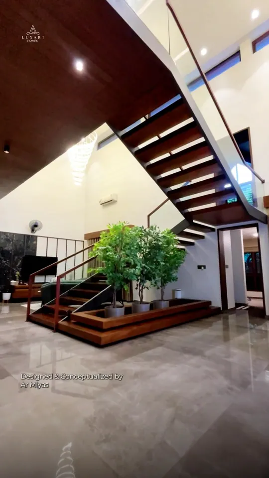 A floating timber staircase with a glass rail in a double-height hall, on the cover of a Luxart Builders reel