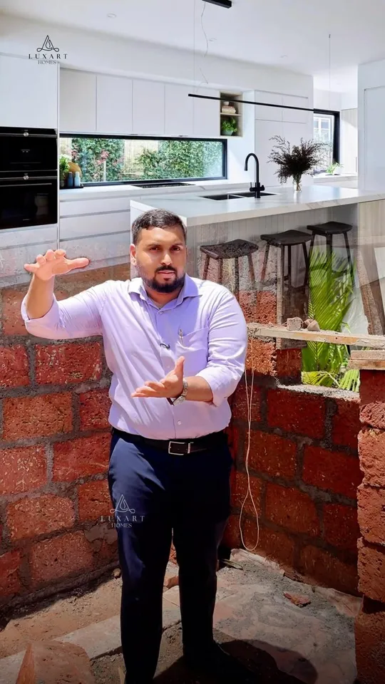A presenter between rising laterite walls, with a finished white kitchen shown above them, on the cover of a Luxart Builders reel