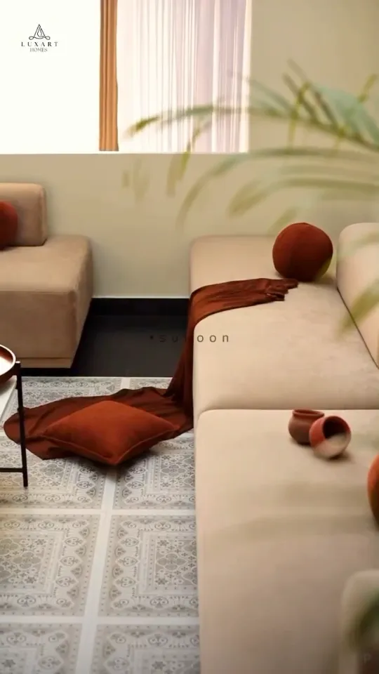 A cream sofa with a rust throw and round cushions on a patterned rug, from a walkthrough reel on the Luxart Builders website
